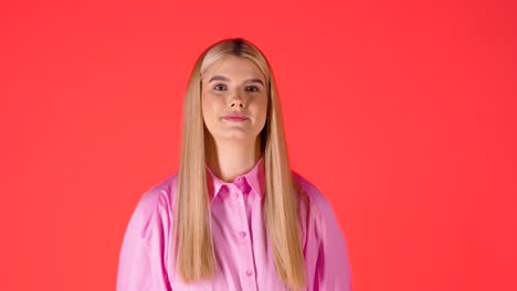 Mujer-Bonita-Rubia-Lanzando-Globos-De-Corazón-Púrpura-En-El-Aire-Mientras-Mira-La-Cámara,-Foto-De-Estudio-Con-Fondo-Rojo.