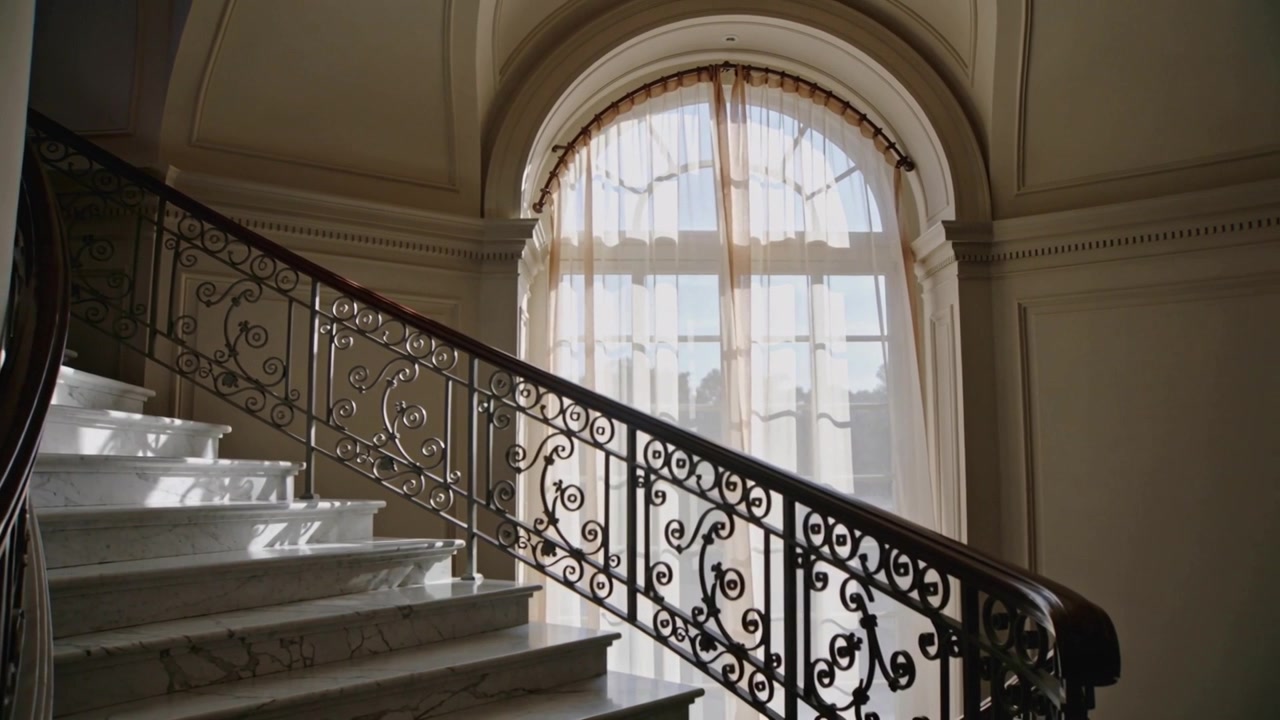 Panning camera revealing marble staircase and iron railing in foyer, centering arched window