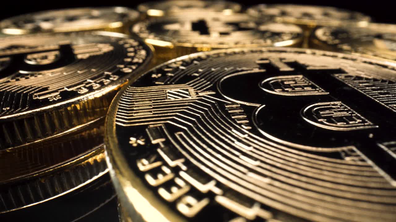 vista macro gran angular bitcoins dorados girando sobre una superficie de vidrio reflectante, fondo negro, inversión en criptomonedas 4k