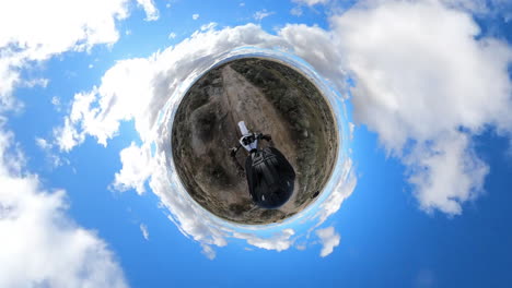 person riding a dirt bike or motorcycle on a tiny planet with a blue sky and cloudy atmosphere