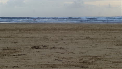 Late-Afternoon-wide-pan-Shot-of-Lifeguard-and-Lifeboat-Searching-for-Swimmers-as-Waves-Splash