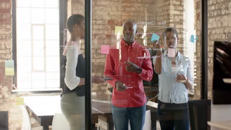 happy african american colleagues taking notes on glass wall and discussing work, slow motion