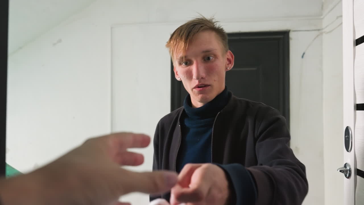 Un uomo bianco riceve una consegna alla porta, scambio con il corriere sul pianerottolo del corridoio, consegna del pacco e di un piccolo articolo, il destinatario sorride mentre si allunga, giacca casual e chiavi visibili vicino alla serratura, interno