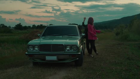 two women dancing near a vintage car at sunset