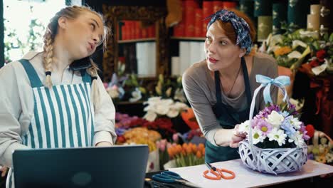 female teenage florist receives orders by the phone while her mom works on decorating a flower basket in her flower shop