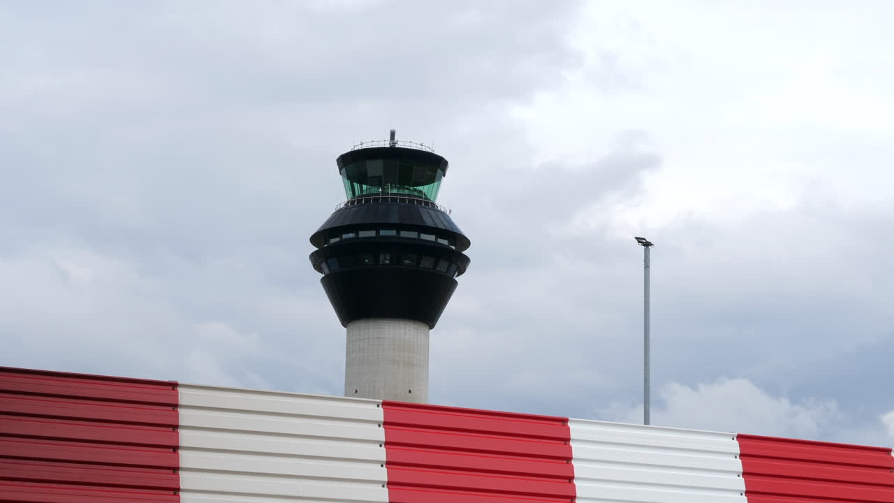 torre de control del tráfico aéreo del aeropuerto con valla roja y blanca en primer plano