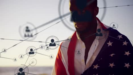 Animation-of-network-of-connections-with-people-icons-over-man-wrapped-in-american-flag-by-sea