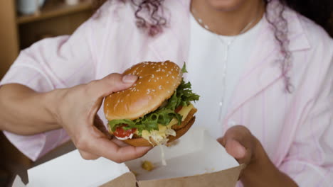 close-up of hands holding a burger in a takeaway box