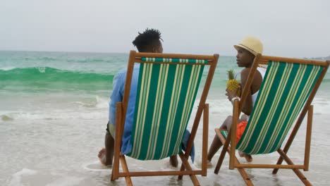 vista trasera de una pareja afroamericana bebiendo jugo de piña en la playa 4k