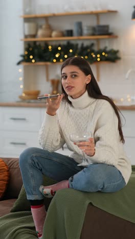 una mujer joven relajándose en casa hablando por teléfono y disfrutando de un martini durante las vacaciones de navidad.