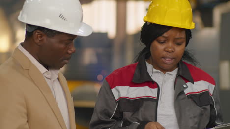 african american colleagues in hardhats talking in factory