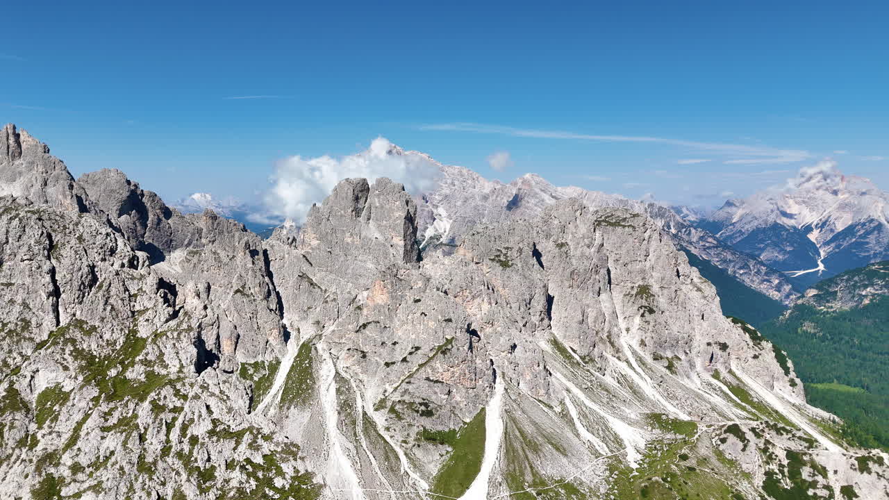 Dik gri kayalıklar ve aşağıdaki alpin vadilerle dramatik Dolomit Dağları'nın hava dron görünümü. Bulutlar kuzey İtalya'nın engebeli zirveleri üzerinde süzülüyor.