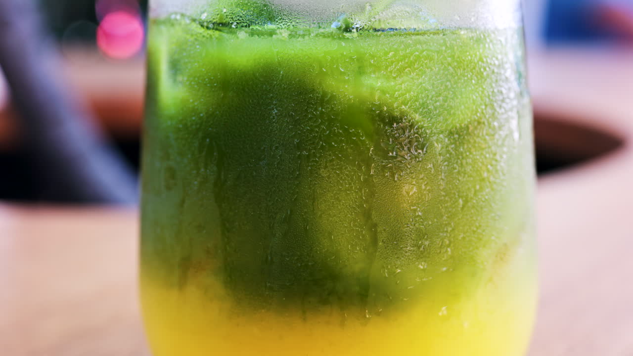 Close up of a glass of an iced orange juice matcha on a table at a cafe