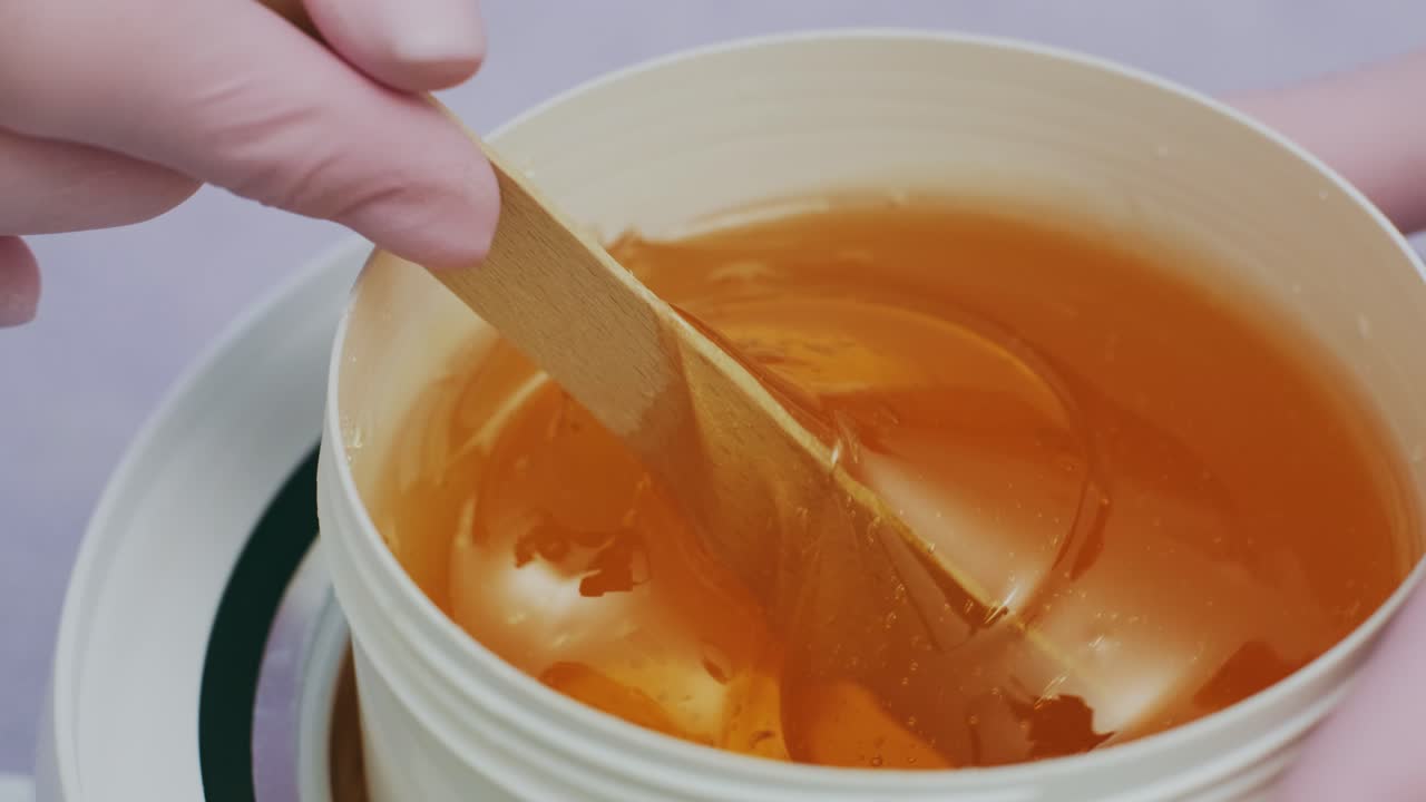 azúcar líquido para la depilación de la piel. toma de primer plano. depilación y concepto de belleza - pasta de azúcar o miel de cera para la eliminación de cabello con palos de espátula de cera de madera