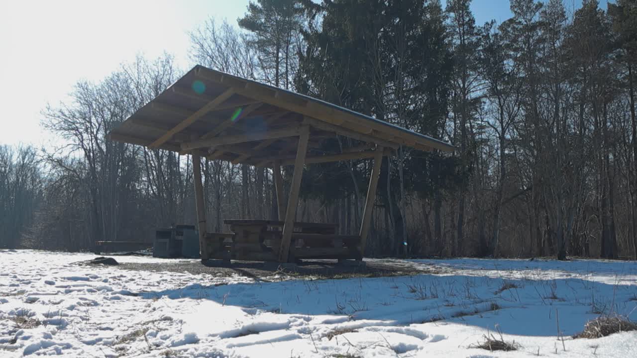 Low perspective of a campfire site with wooden sheltered picnic table, serving as a rest stop in Tabasalu Nature Park on a sunny winter day. Snow covered landscape. Winter weekend get a away in nature