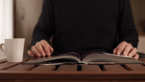 caucasian man is studying for university while drinks a cup of tea or coffee on a wooden table