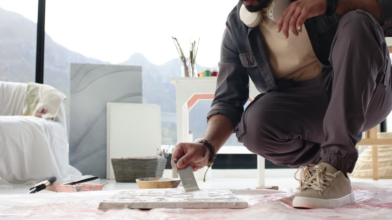 Triggered by paint scoop, artist is dragging knife across grid of canvases to achieve coverage