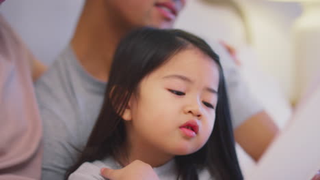 Family-With-Two-Fathers-In-Bed-At-Home-Reading-Story-To-Daughter