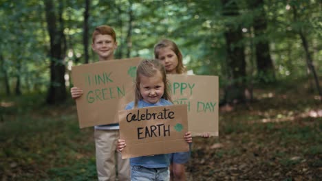 Group-of-kids-holding-posters-and-looking-at-camera-in-forest.