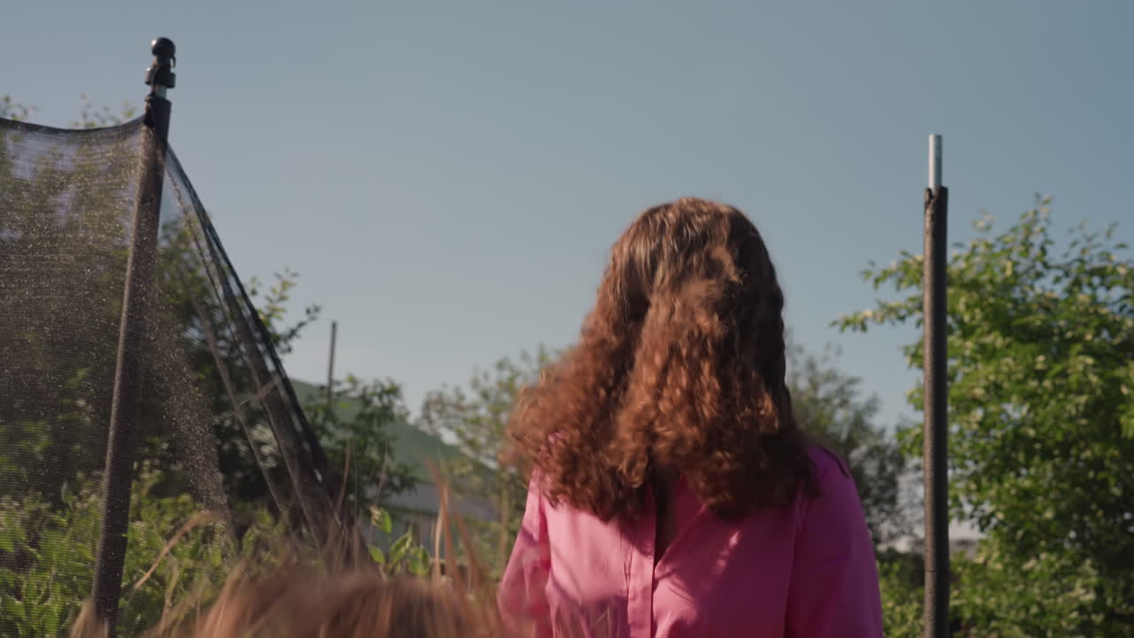 Girls Spinning By Trampoline Outdoors, Two Young Sisters Enjoying Energetic Moments In Natural Surroundings, Sisters Sharing Cheerful Playtime In Backyard Near Trampoline Beneath Cloudless Sky