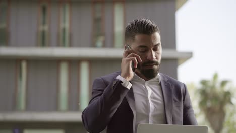 Serious-businessman-using-smartphone-and-laptop-outdoor