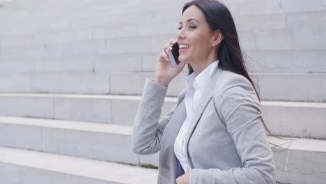 Lachende-Frau-Sitzt-Auf-Der-Treppe-Mit-Telefon