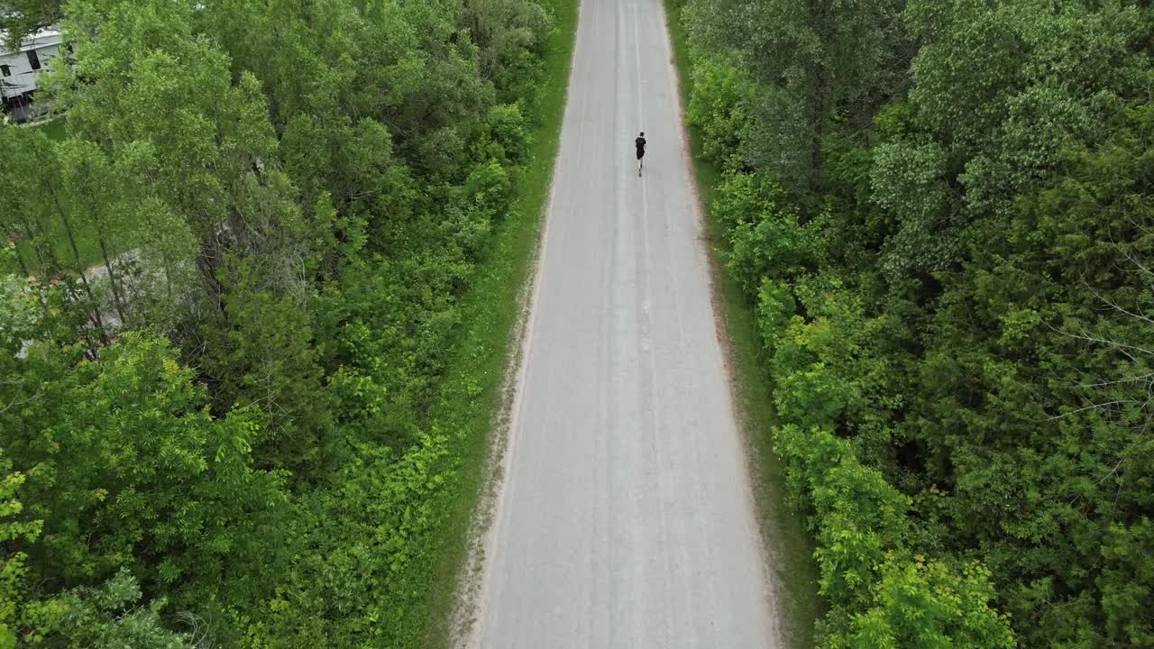 Lone Person Running On The Isolated Road Passing By Trees With Green Lush Foliage