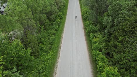 Persona-Solitaria-Corriendo-En-La-Carretera-Aislada-Que-Pasa-Por-árboles-Con-Follaje-Verde-Y-Exuberante