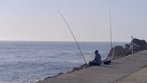 man fishing on the harbor break wall in the town of nazare, portugal