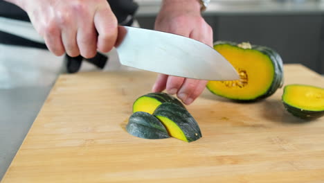 male chef roughly chopping big slices of green pumpkin on the kitchen with the sharp knife