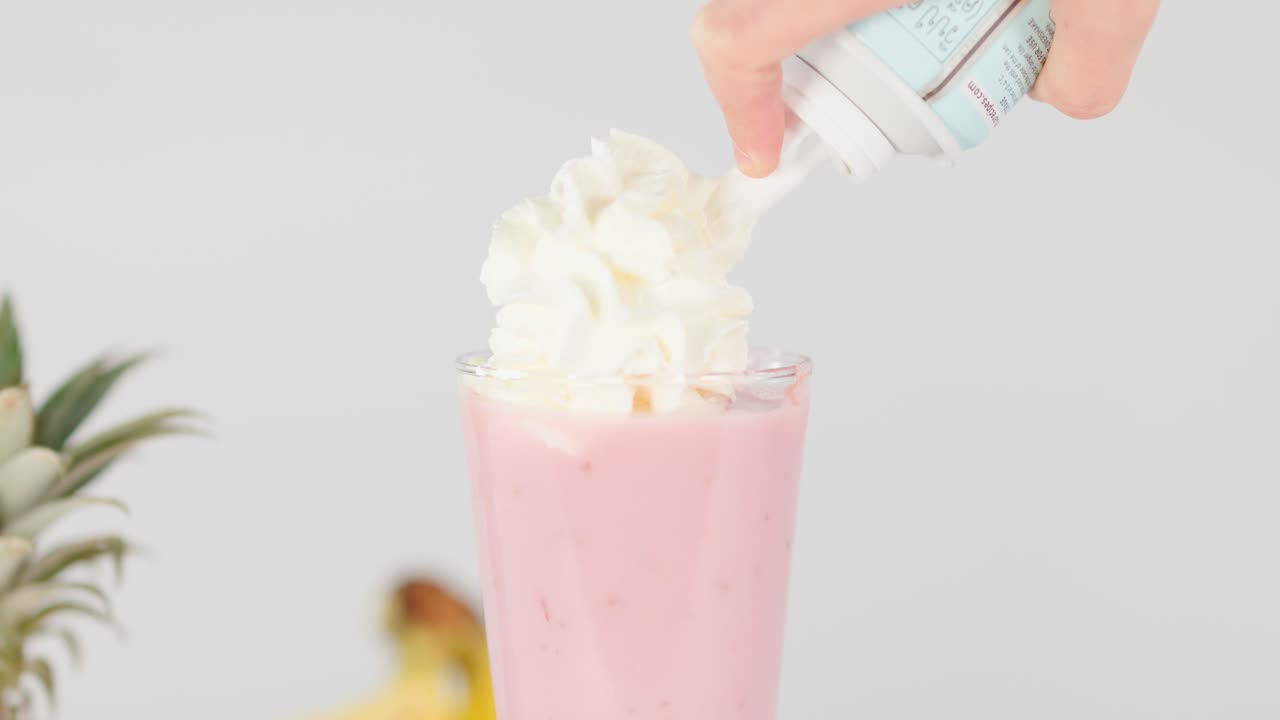 Hånd påfører pisket krem på rosa fruktsmoothie i glass, sterkt studiolys, statisk bilde