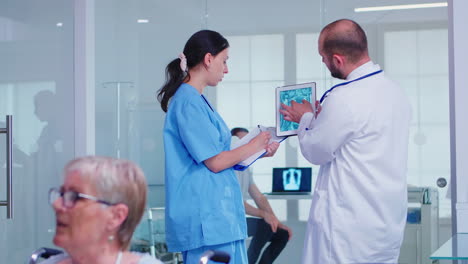 Medical-staff-holding-tablet-pc-with-patient-radiography-in-hospital-hallway