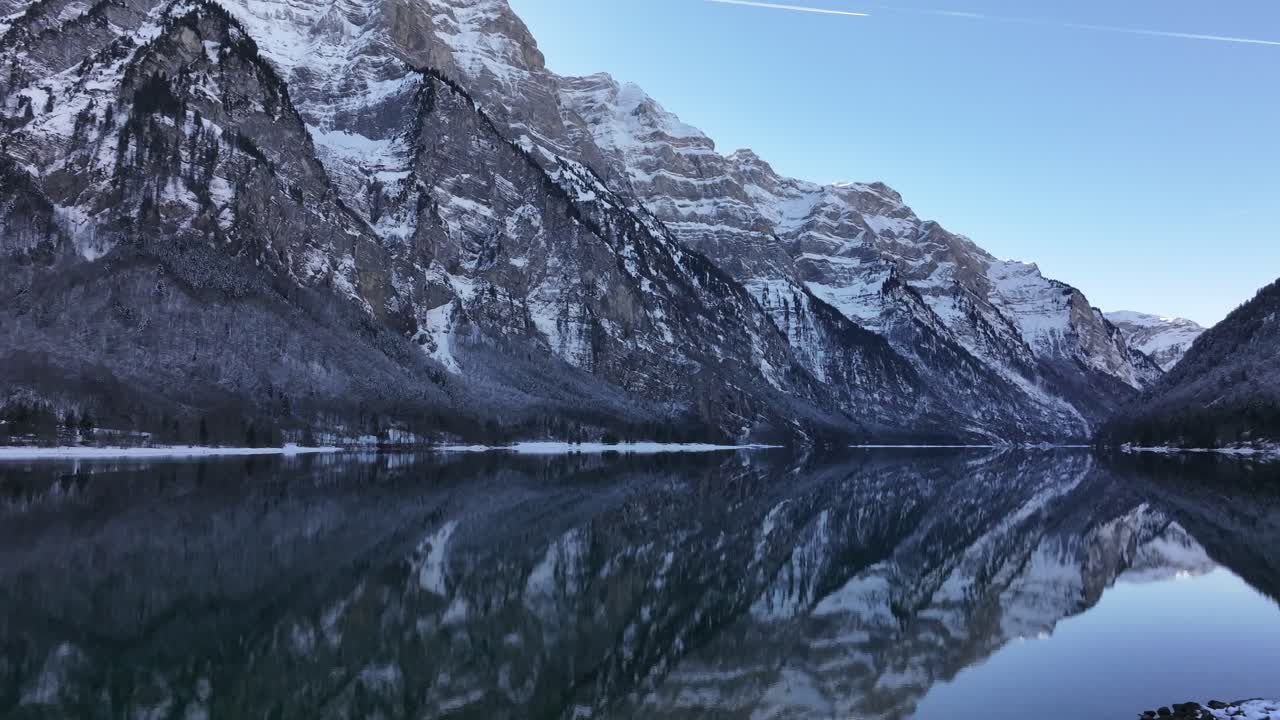 Breathtaking aerial view of Klöntalersee lake on a winter day, with the surrounding mountains perfectly mirrored in the water.