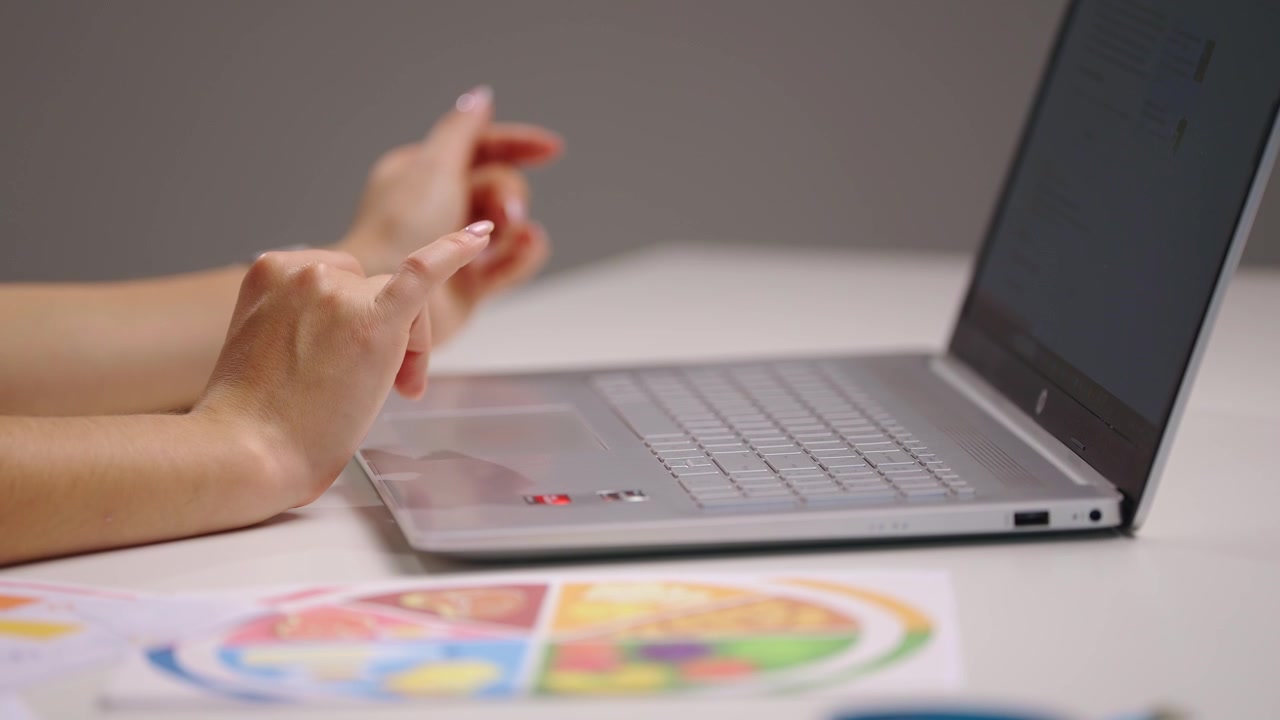 Vista laterale ravvicinata di mani femminili che cliccano e scorrono su un laptop mentre esaminano grafici e diagrammi colorati, creando un'analisi dei dati nutrizionali e pianificando un programma di dieta sana personalizzato
