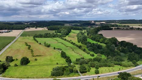 puffy dense clouds over green farm fields and hills of american suburb. driving cars on interstate intersection in summer. aerial lateral wide shot