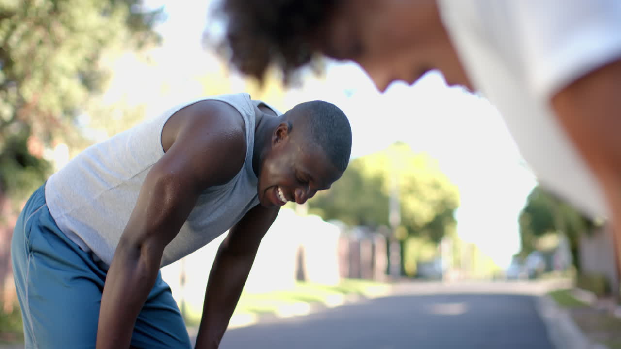 Exercising outdoors, two multiracial male friends resting after running on sunny day, copy space