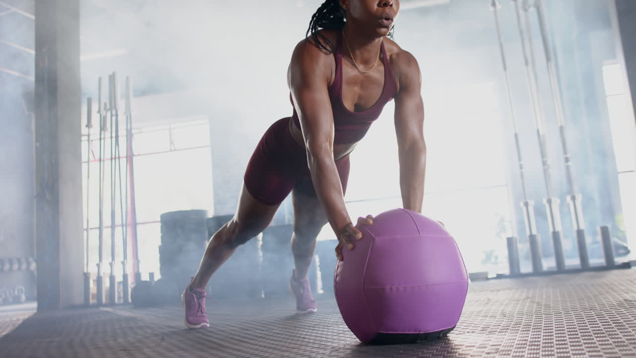 Exercising in gym, woman doing push-ups with purple medicine ball