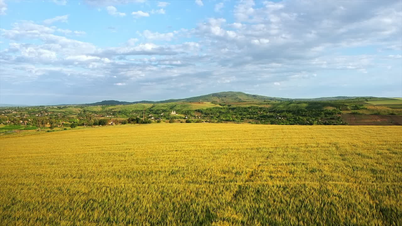 Aerial drone view of a village in Moldova at sunset. Wide field, residential buildings, church, narrow river, greenery, hills in the distance