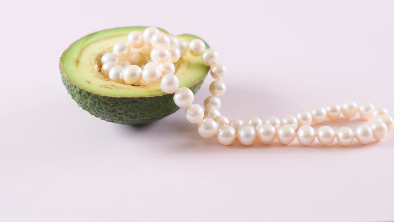 la mitad de un aguacate con perlas en un fondo rosa claro. surrealismo. diseño de alimentos de moda