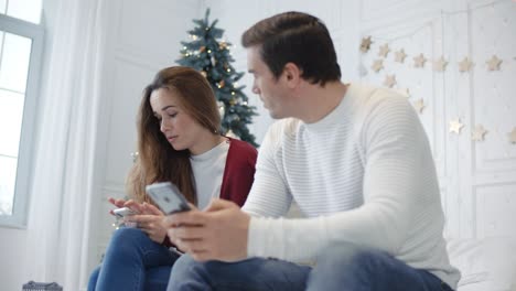 Ernsthaftes-Paar-Sitzt-Mit-Mobiltelefonen-Im-Luxusschlafzimmer.