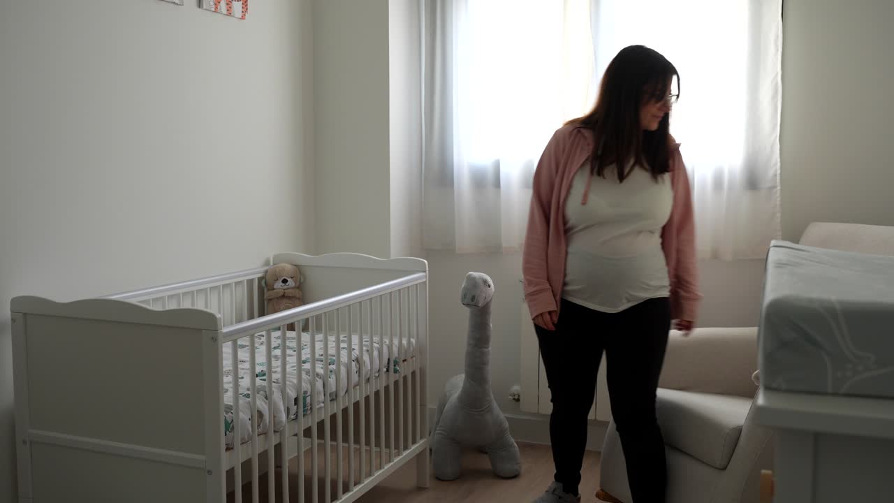 Pregnant woman caressing a stuffed dinosaur in future baby room