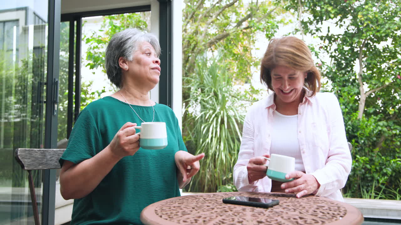 Senior women enjoying coffee and conversation on patio, surrounded by greenery