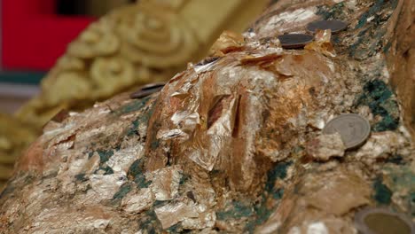 Close-up-view-of-Buddha-statue-with-offering-of-coins-for-good-luck-at-Buddhist-temple,-Thailand