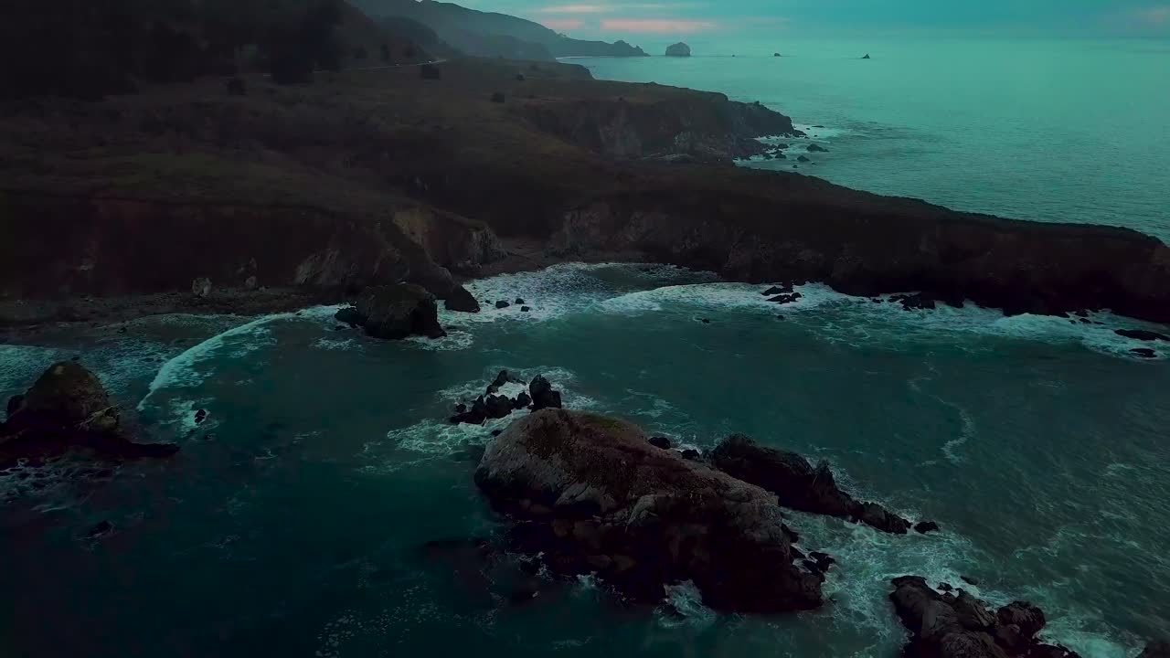 Fast dolly out reveal of huge ocean cliff peninsula eroded by crashing waves at dusk at Sand Dollar Beach in Big Sur California