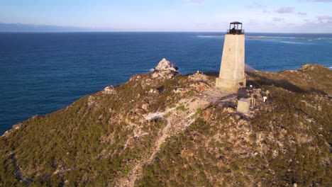 a solitary lighthouse on a rugged coastline with ocean backdrop, clear sky, aerial view