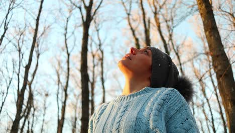 caucasian-girl-looks-at-the-trees-in-the-forest-at-sunset,-slow-motion-shot