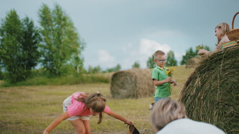 back view close up of woman and little girl spreading checkered blanket in open farmland with people standing nearby under cloudy sky, outdoor picnic preparation in serene rural countryside setting