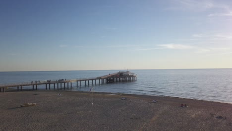 Drone-Despegando-Sobre-Un-Muelle-Durante-La-Hora-Dorada-Revelando-Un-Vasto-Mar-Azul