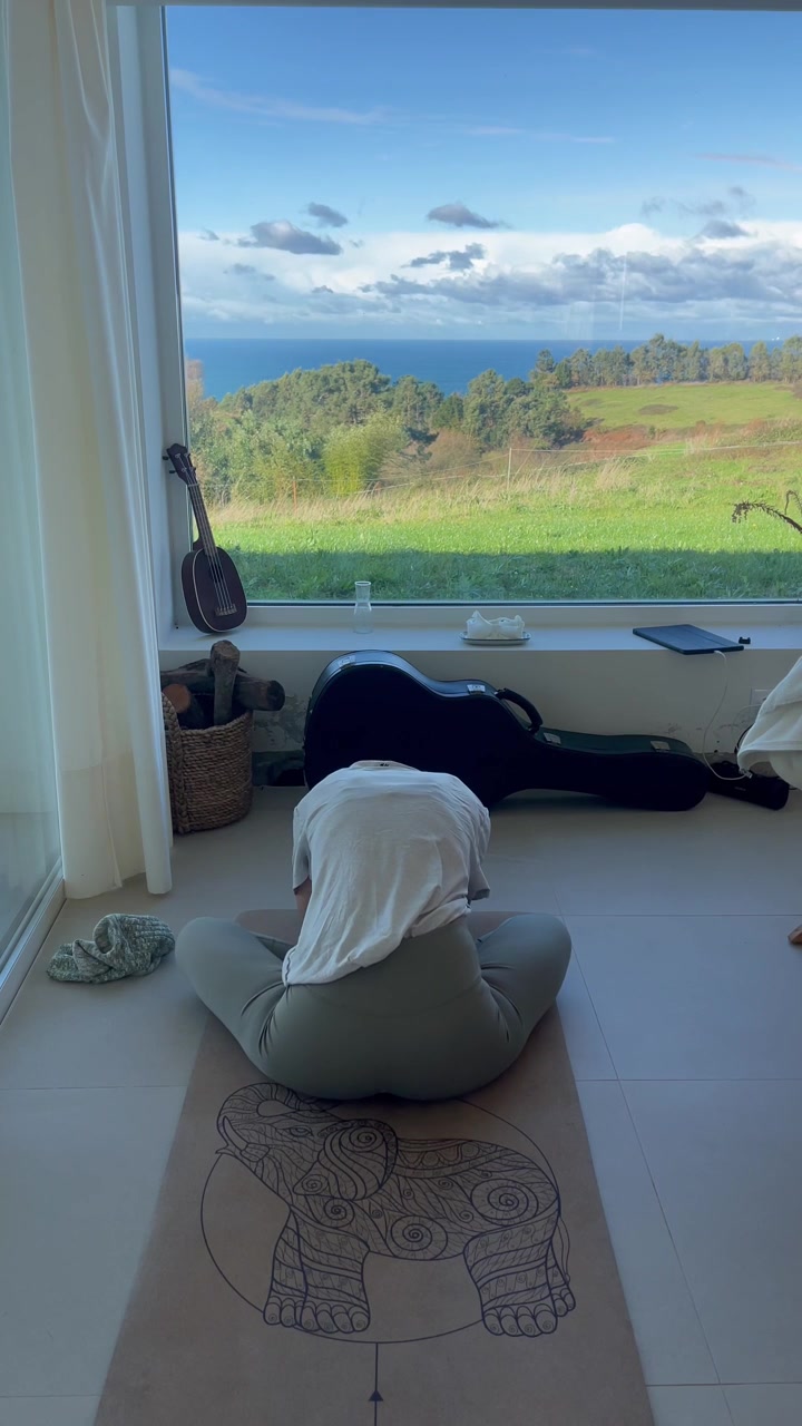 Video verticale di una donna che si piega in avanti su un tappetino da yoga accanto a una finestra con vista mare.