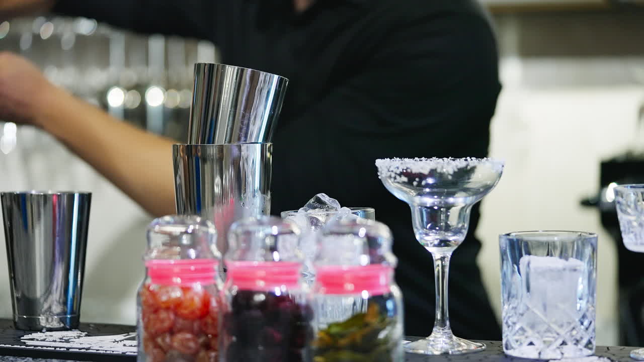 Male bartender wearing black shirt making cocktails. Professional using metal cups to mix the beverages.